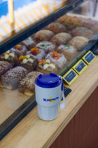 White tumbler with blue lid featuring 'Blue Moon' logo on a counter with pastries in the background.