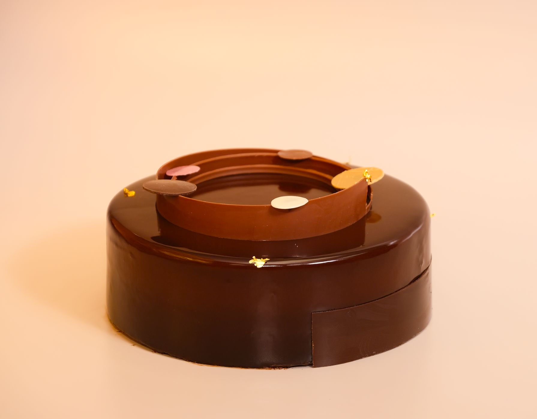 Round glazed chocolate mousse cake with decorative elements on a pink background with editable gold leave top and chocolate disks