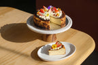 Best Original Basuqe Cheesecake with a slice on a stand on a wooden table, at Blue Moon Bakehouse, in Christchurch New Zealand